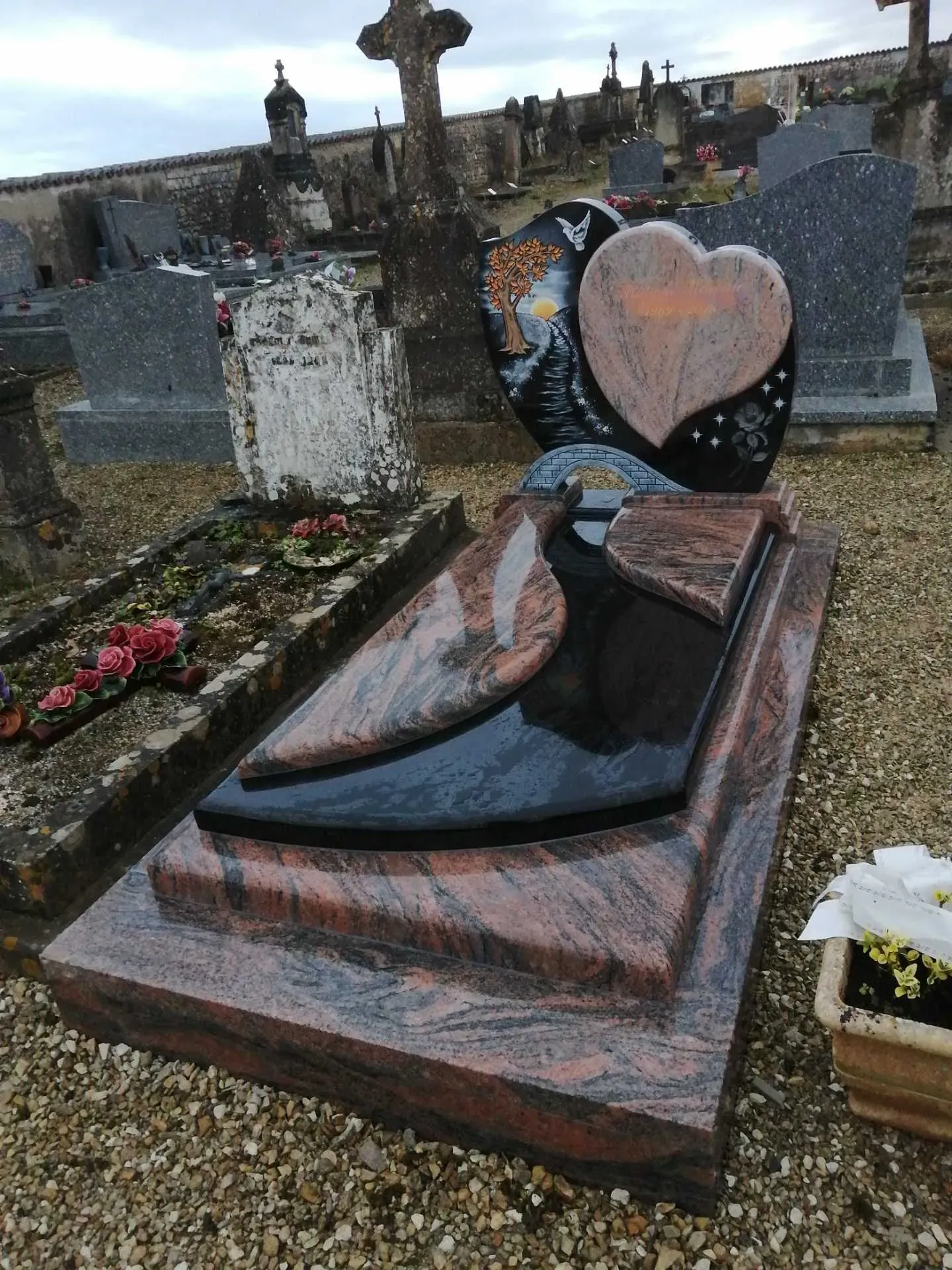 Monument funéraire en granit bicolore avec stèle en cœur gravée dans un cimetière.