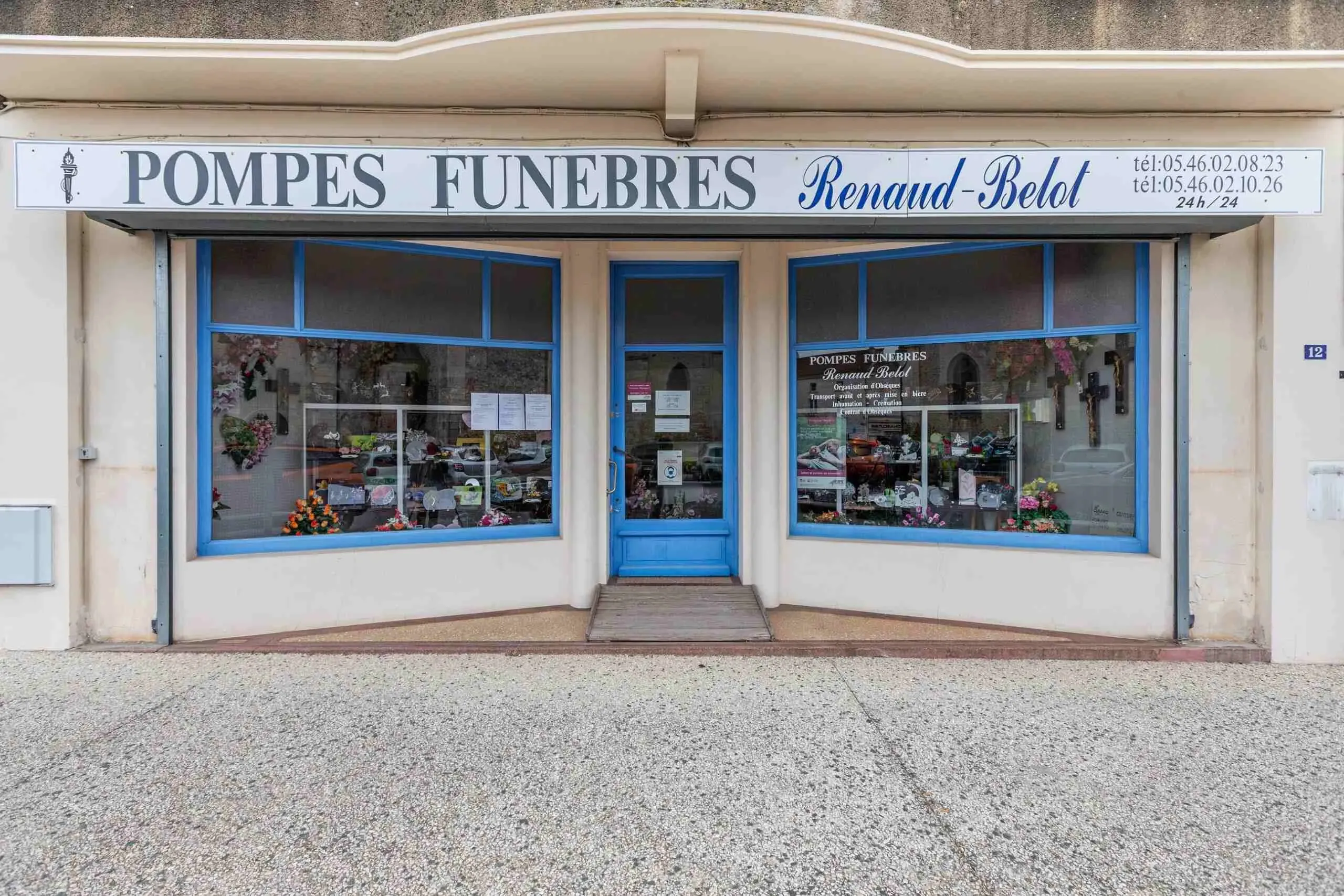 Façade bleue des Pompes Funèbres Renaud-Belot avec vitrines décorées.